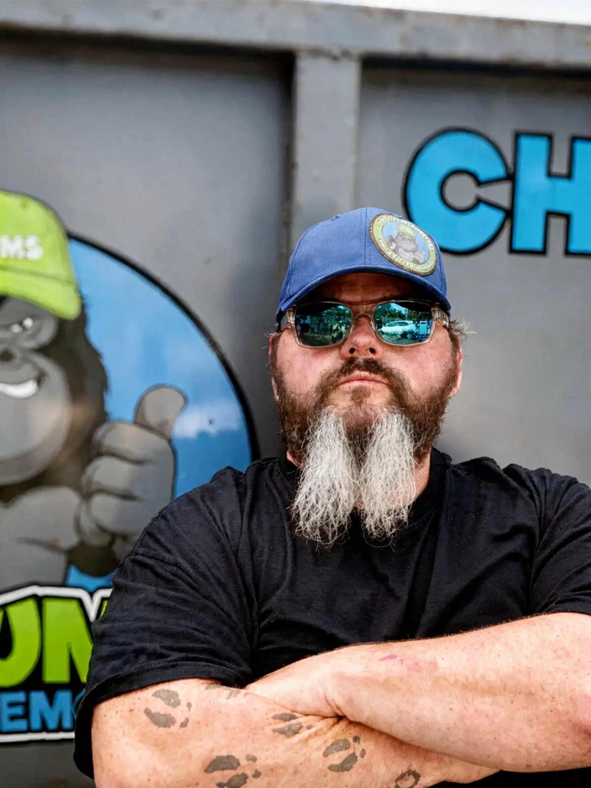 James from the Chums Junk Removal crew, arms crossed in front of the company's branded gorilla-logo trailer